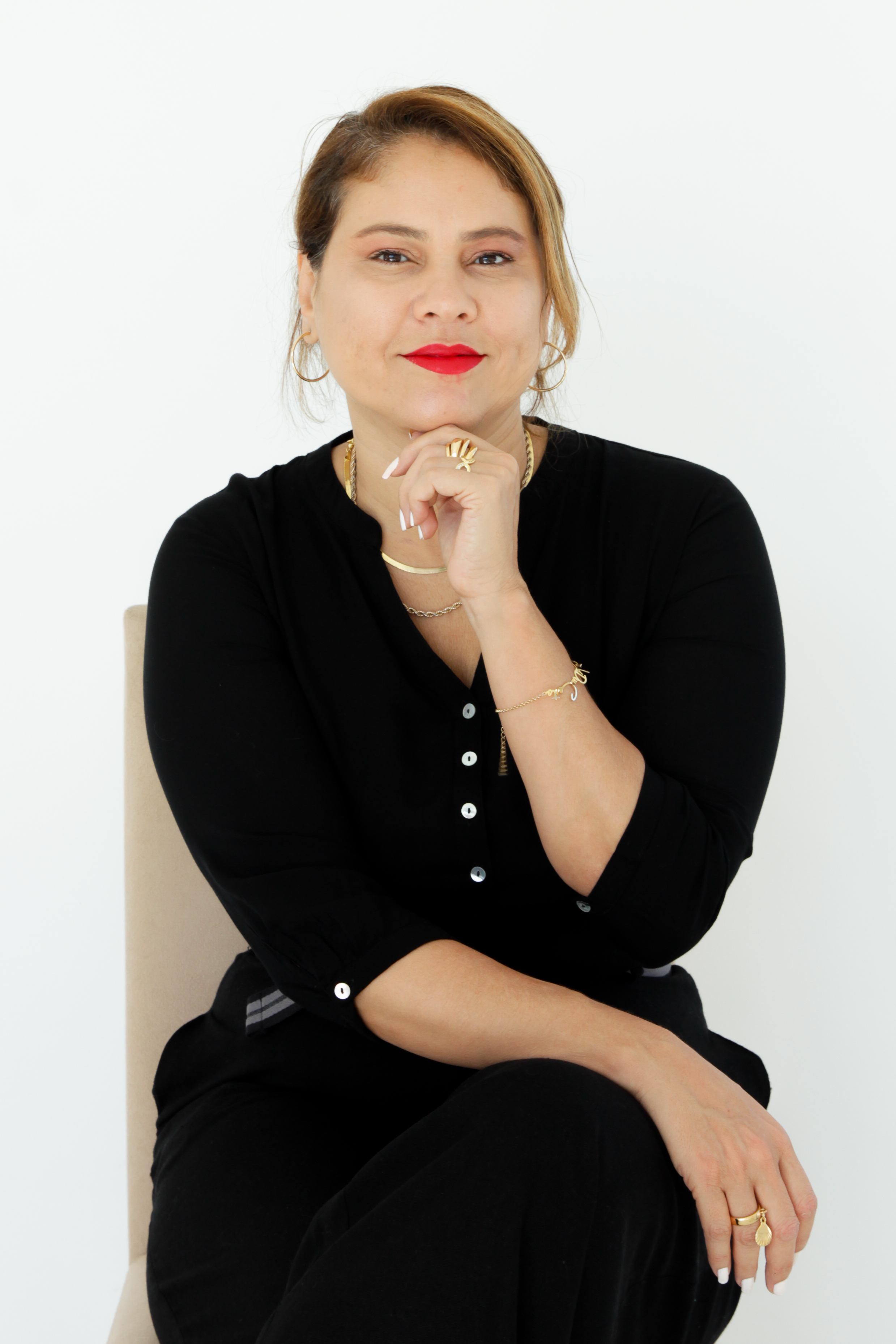 Jaqueline Salles sentada, com roupa preta, apoiando o queixo na mão.